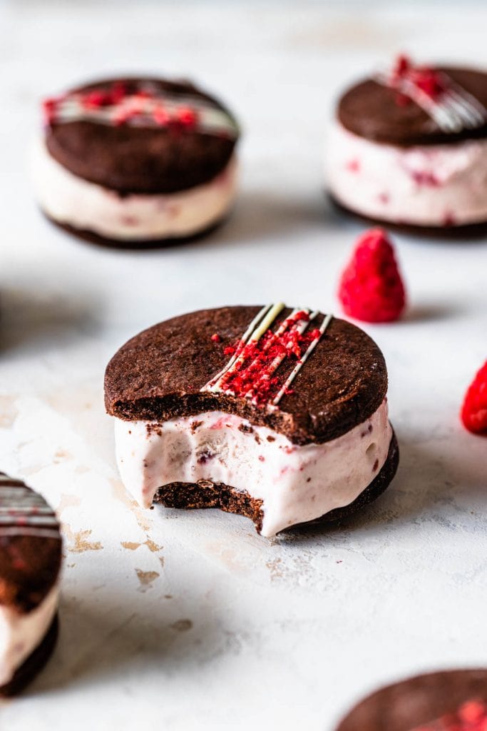 Chocolate Raspberry Ice Cream Sandwiches with a bite taken out, topped with chocolate drizzle and freeze dried strawberries