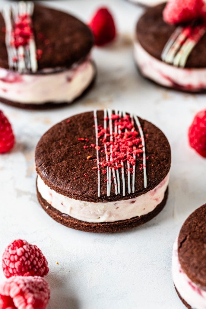 Chocolate Raspberry Ice Cream Sandwiches in a pan two sandwiches stacked. topped with chocolate drizzle and freeze dried raspberries