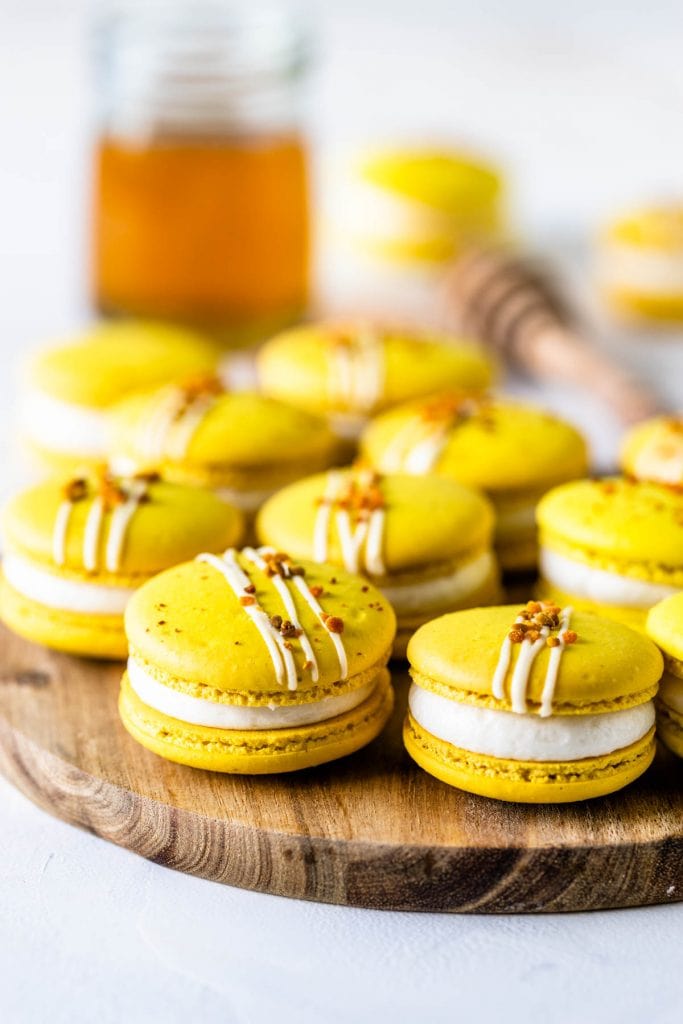 yellow Macarons topped with bee pollen on a wooden board with a jar of honey on the back