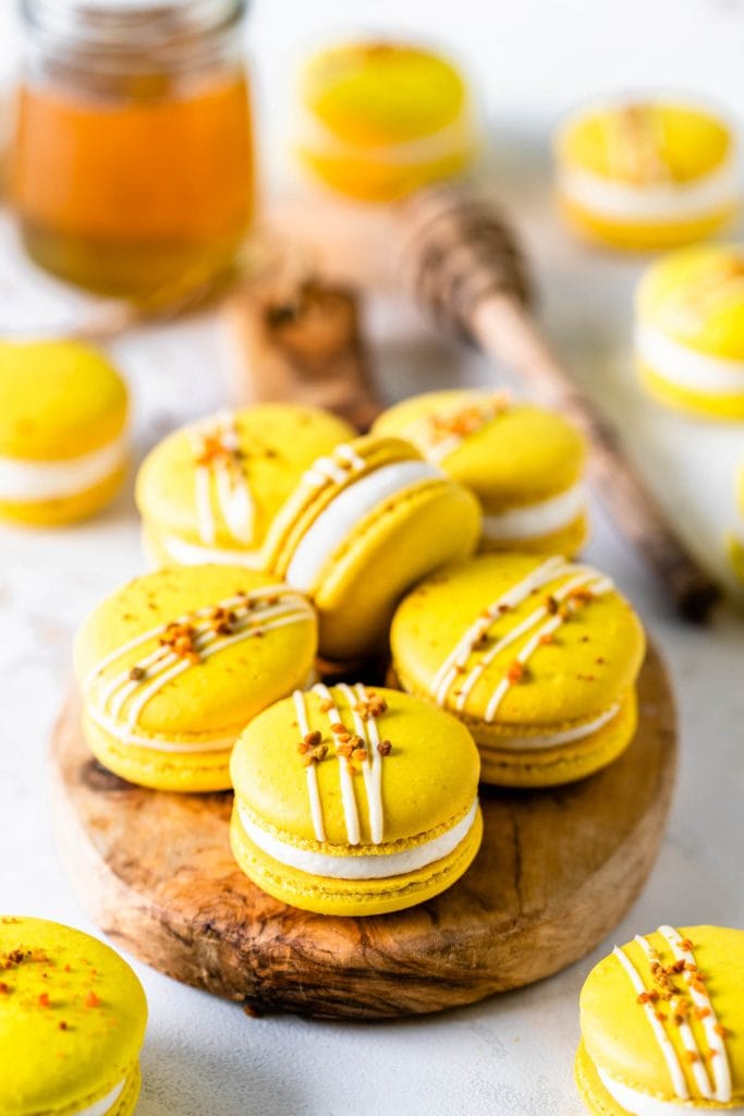 Honey Macarons topped with bee pollen on a wooden board with a jar of honey on the back