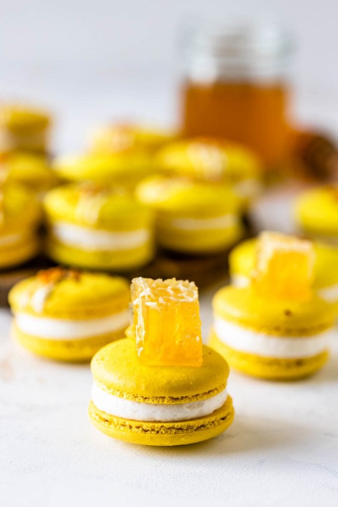 yellow Macarons topped with a piece of honey comb on a wooden board with a jar of honey on the back