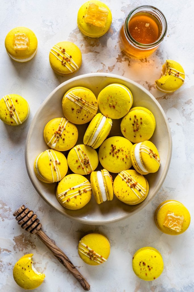 Honey Macarons topped with bee pollen in a plate, seeing from the top, with a jar of honey on the side, and a honey spoon