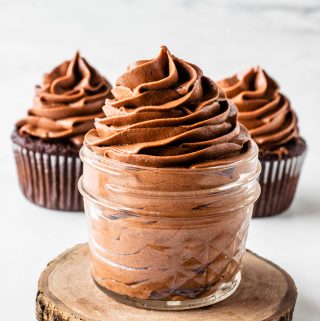 Nutella frosting piped in a small mason jar, with two cupcakes frosted with Nutella frosting on the background