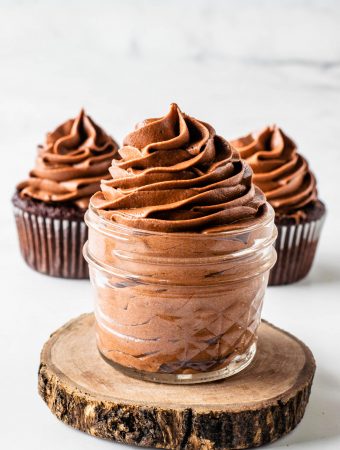 Nutella frosting piped in a small mason jar, with two cupcakes frosted with Nutella frosting on the background