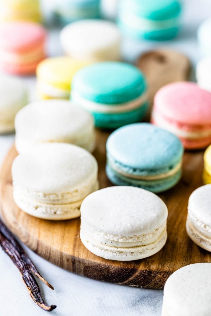 white, blue, teal, pink and yellow macarons on top of a wooden board