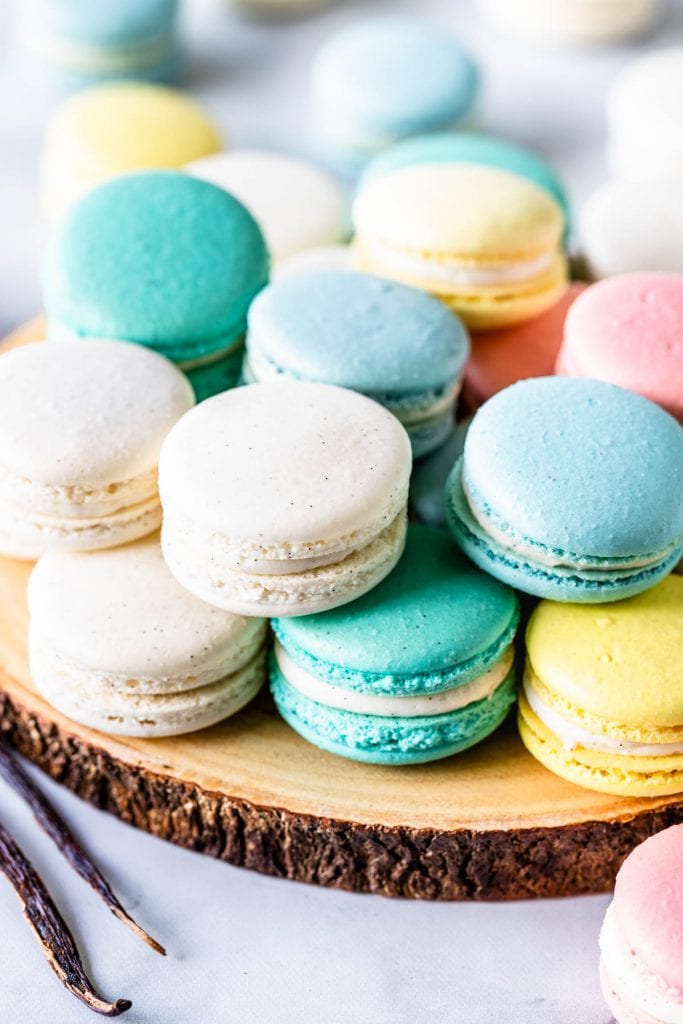 white, blue, teal, pink and yellow macarons on top of a wooden board