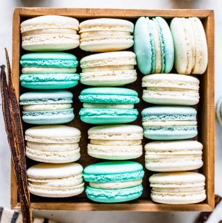 Vanilla Bean Macarons, green, white, blue, in a box, viewed from the top, with a vanilla pod on the side