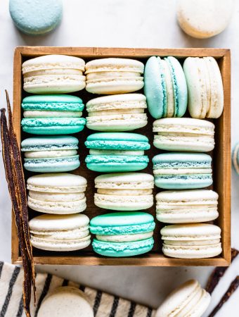 Vanilla Bean Macarons, green, white, blue, in a box, viewed from the top, with a vanilla pod on the side