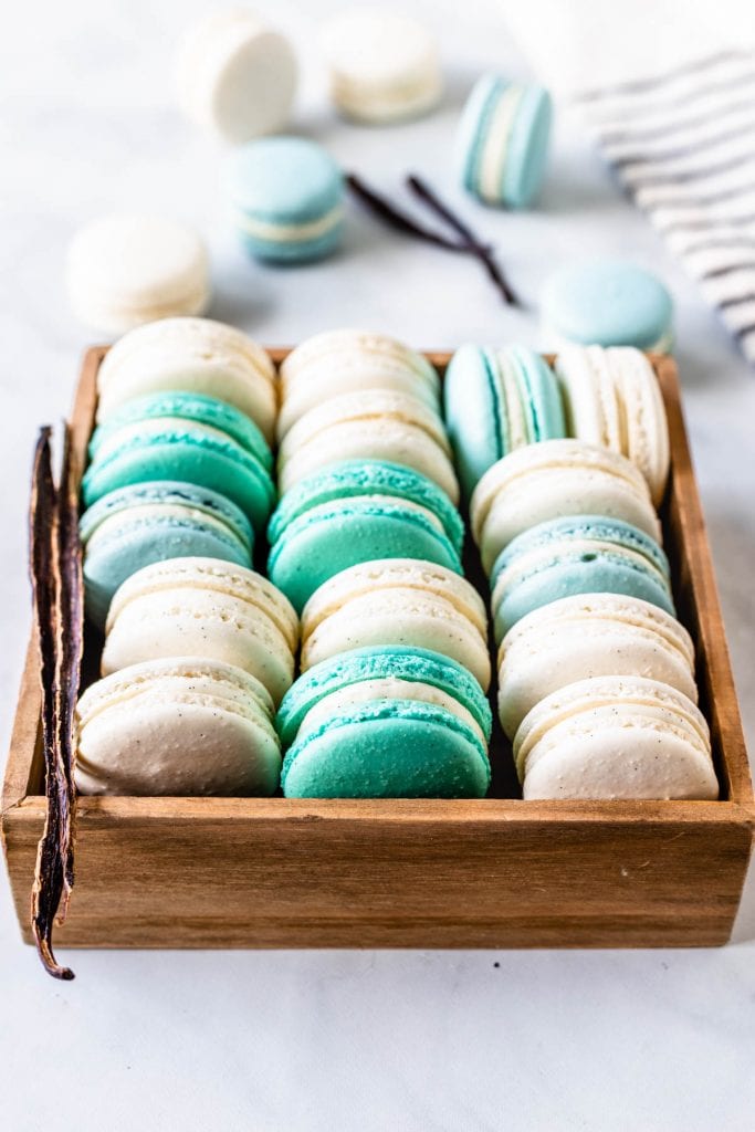 Vanilla Bean Macarons, green, white, blue, in a box, with a vanilla pod on the side
