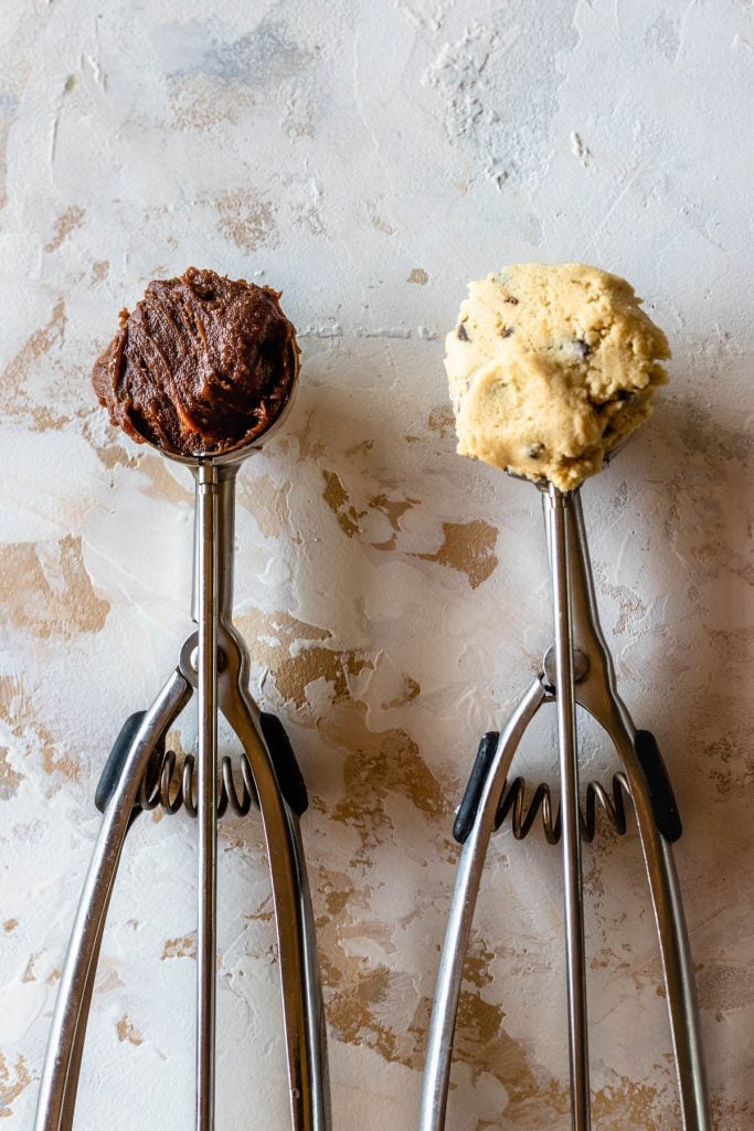 two cookie scoops one with brownie batter and the other with chocolate chip cookie dough
