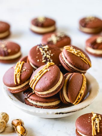 chocolate macarons with peanut butter filling in a bowl, with drizzled peanut butter and chocolate on top