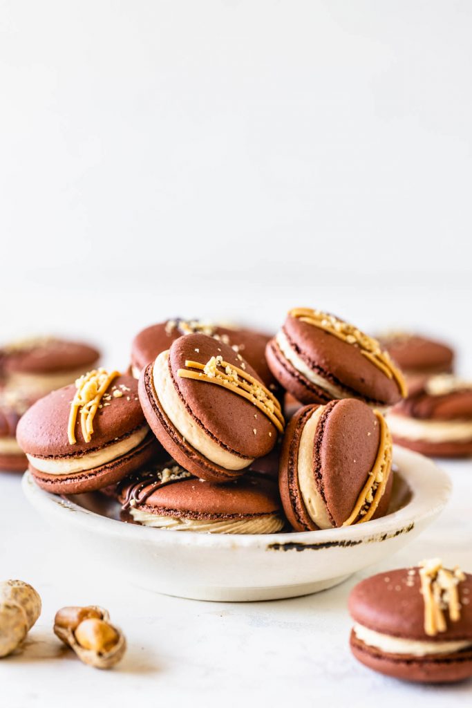 Peanut Butter Macarons topped with peanut butter drizzle and chopped peanuts in a bowl