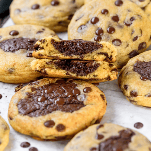 Stacked brookie cookies showing the thick brownie center inside soft chocolate chip cookie dough, with chocolate chips scattered on top.