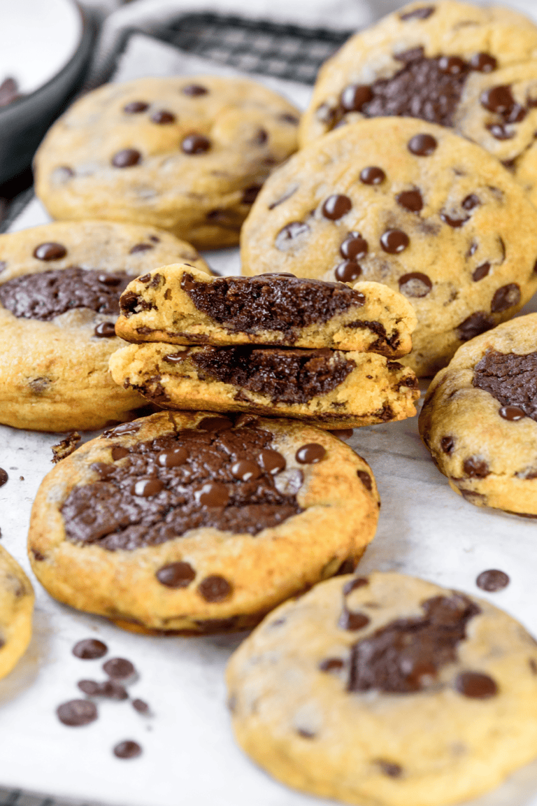 Stacked brookie cookies showing the thick brownie center inside soft chocolate chip cookie dough, with chocolate chips scattered on top.