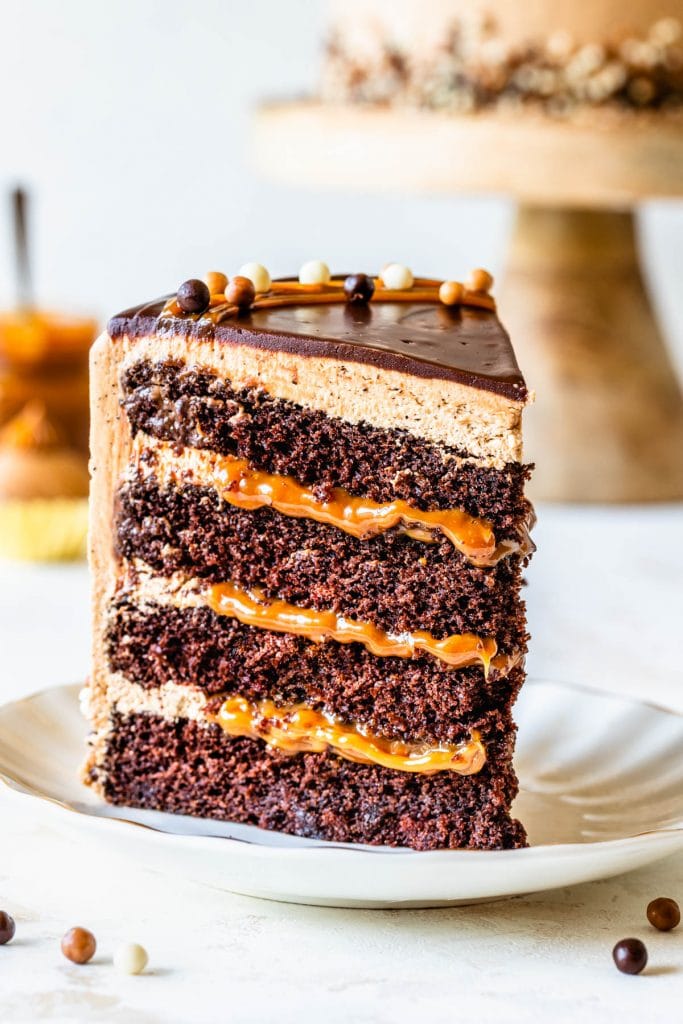 slice of chocolate cake filled with dulce de leche, topped with mocha buttercream and chocolate ganache, and crispearls