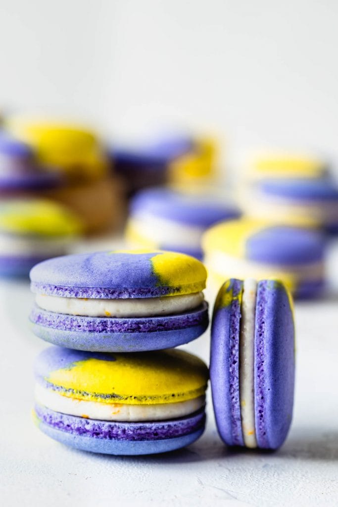 Vegan Lemon Blueberry Macarons purple and yellow shells filled with lemon buttercream, two macarons stacked on top of the other and one macaron on the side