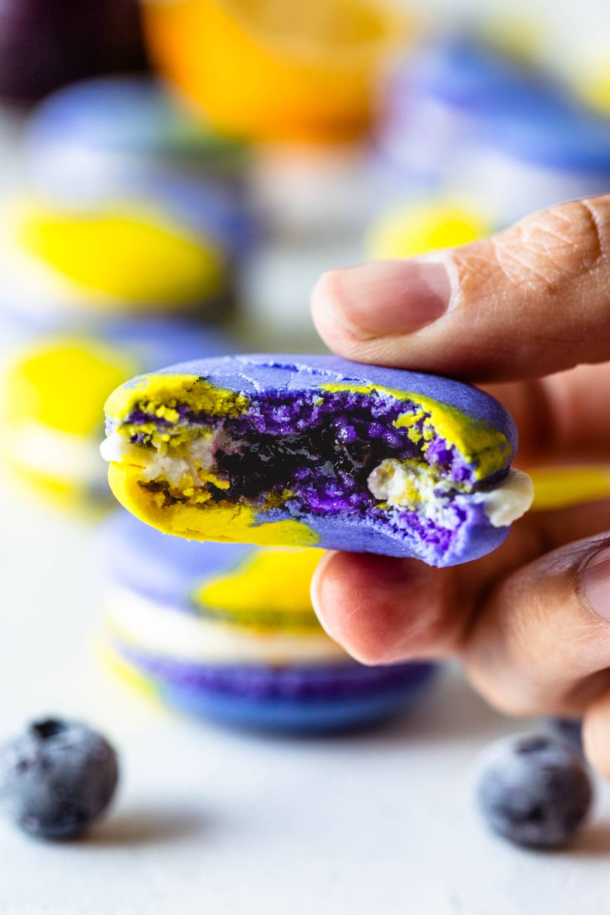 purple and yellow vegan macarons filled with buttercream and blueberry jam, with a bite taken to show the inside of the macarons