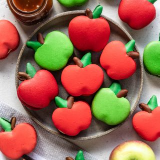 macarons shaped like apples on a plate with caramel sauce on the side and an apple.