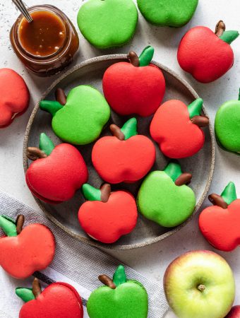 macarons shaped like apples on a plate with caramel sauce on the side and an apple.