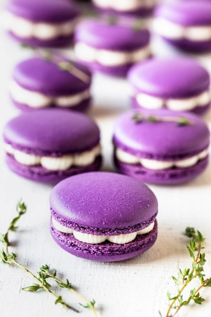 purple macarons filled with fig jam and buttercream, with thyme as a garnish on top.
