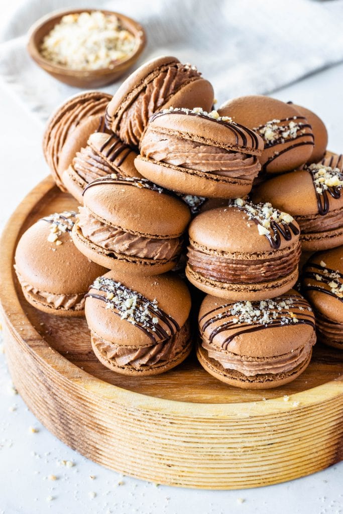 chocolate macaron shells filled with nutella buttercream on top of a round wooden stand.