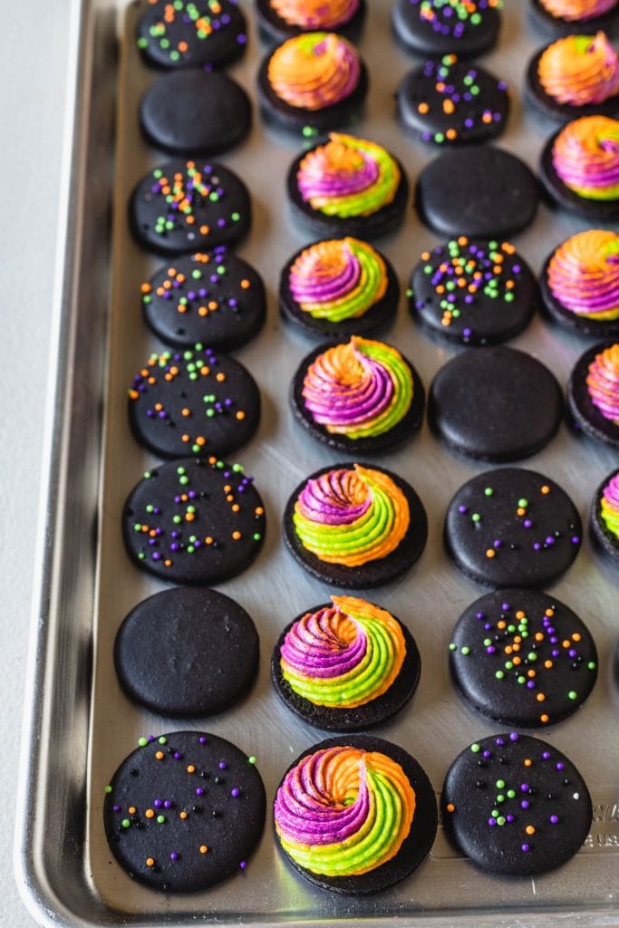 black macaron shells filled with a swirl of tricolor buttercream frosting, and sprinkles on top of the shells.