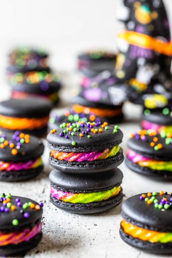 halloween Macarons stacked filled with a purple, green and orange frosting, topped with colorful sprinkles.