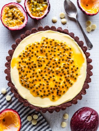 Passionfruit Tart topped with passionfruit seeds with a chocolate crust, and passionfruits around.