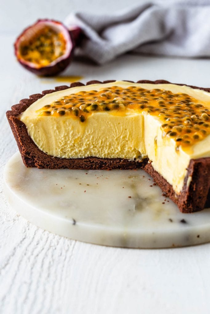 Passionfruit Tart topped with passionfruit seeds with a chocolate crust, and passionfruit in the back.