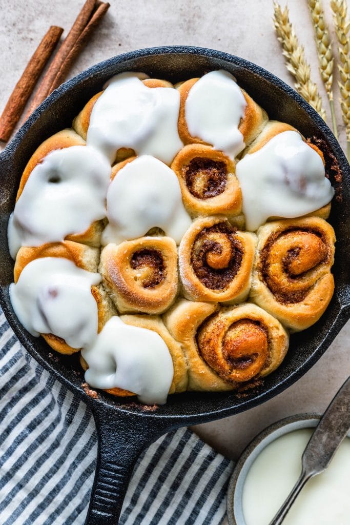 Mini Cinnamon Rolls in a skillet, topped with cream cheese frosting.