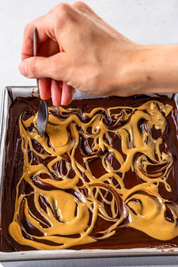 using a spoon to swirl around peanut butter on top of the chocolate ganache.