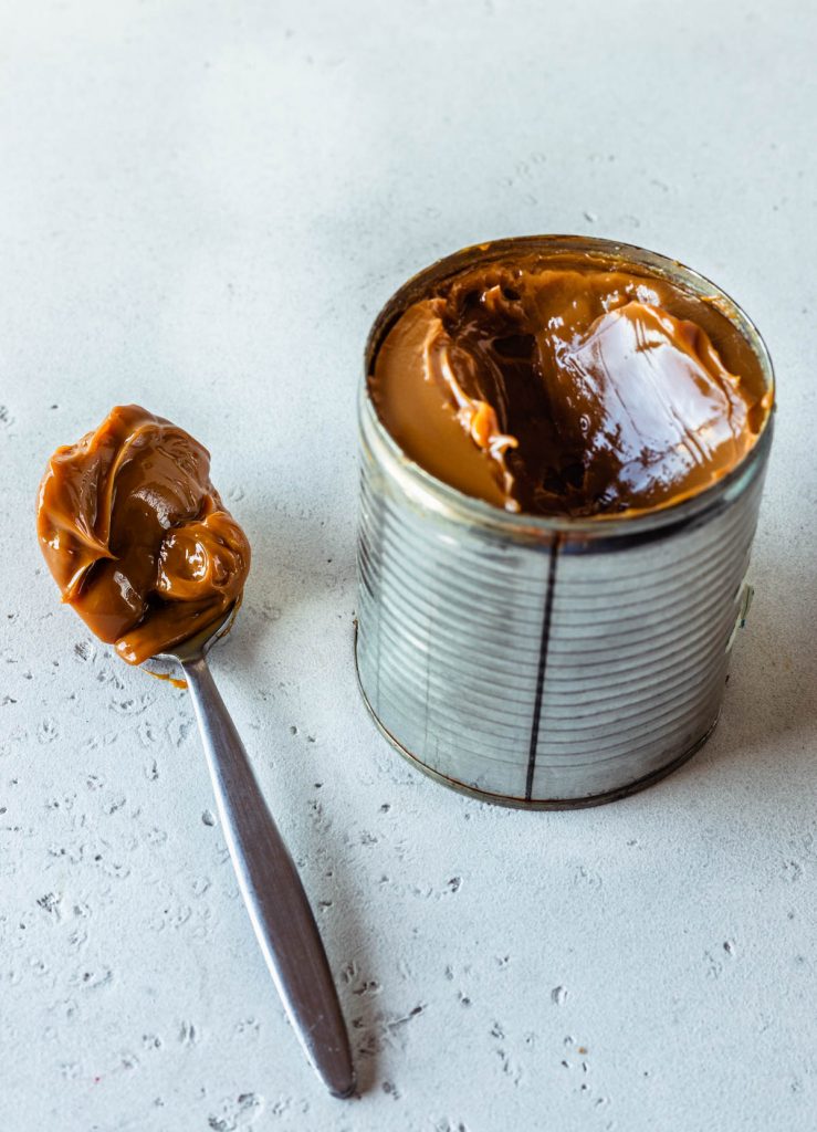 can of dulce de leche opened with a spoon on the side with dulce de leche.