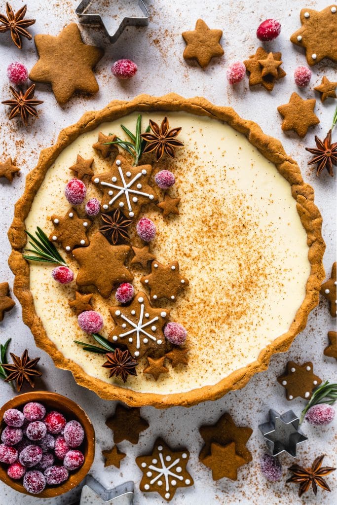 christmas pie filled with eggnog filling and gingerbread crust, topped with gingerbread cookies, sugared cranberries and rosemary sprigs.