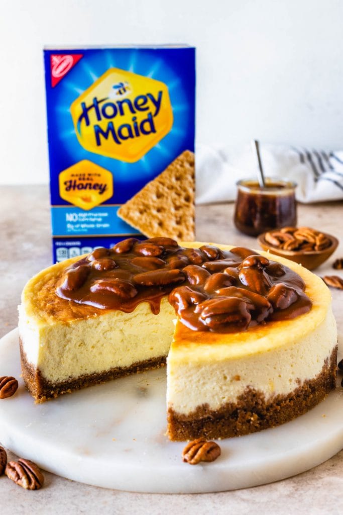Pecan Pie Cheesecake topped with caramel sauce, with a box of honey maid graham crackers in the back.