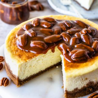 Pecan Pie Cheesecake topped with caramel sauce, with a slice cut out and displayed in the back.