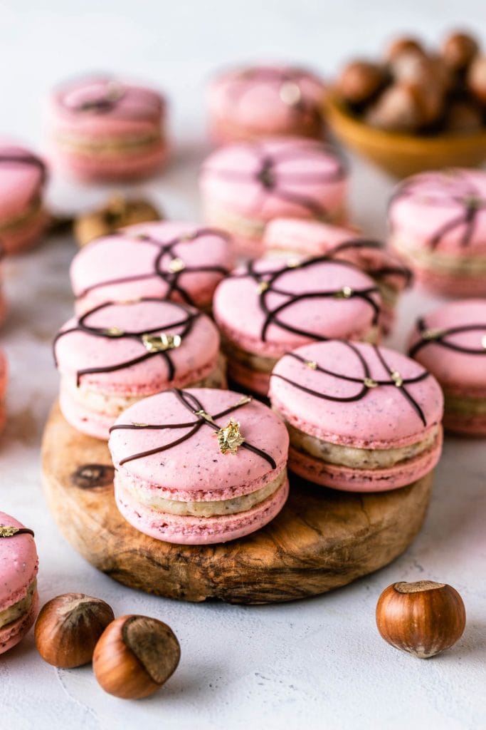 pink macarons with a chocolate decoration on top and golden leaf accents.