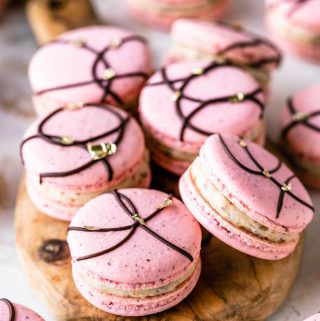 pink macarons with a chocolate decoration on top and golden leaf accents.