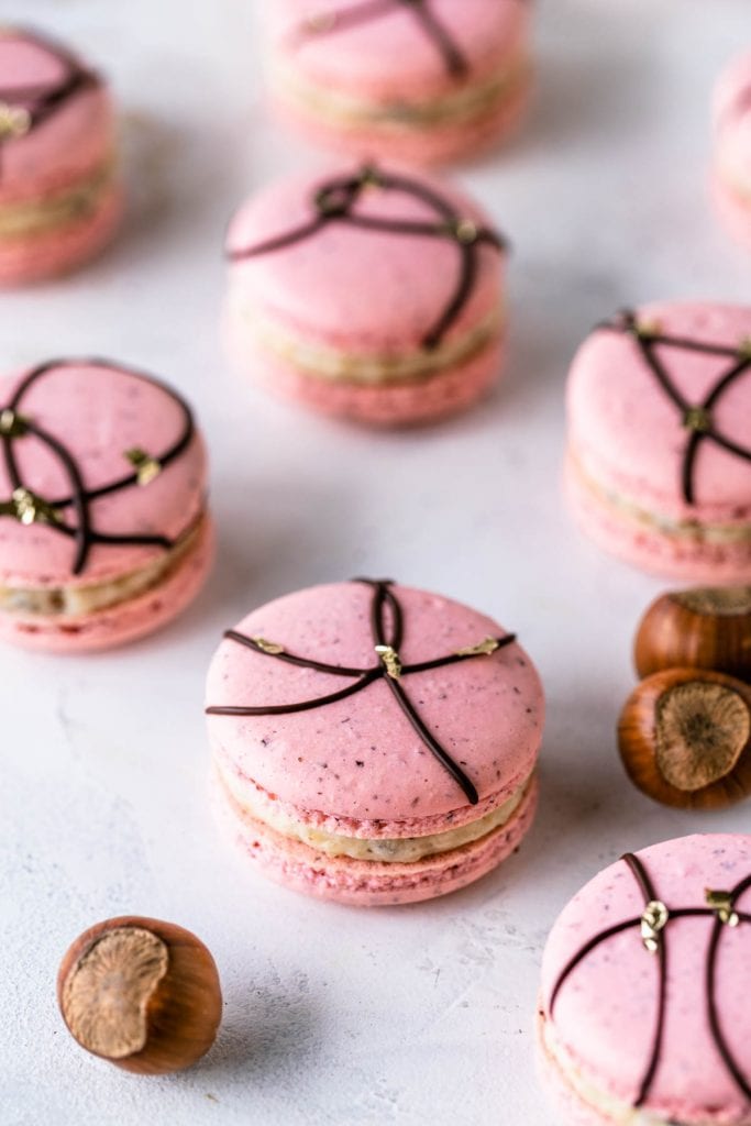 Hazelnut Macarons pink macaron shells with a chocolate decoration on top.