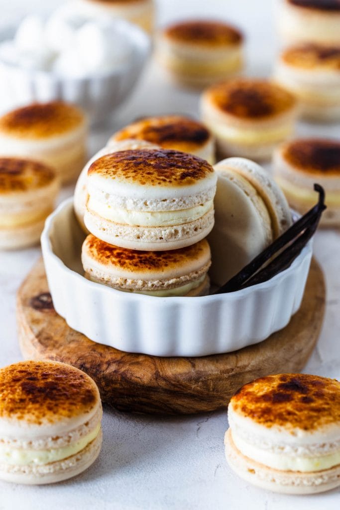 Creme Brûlée Macarons inside of a ramekin, with the tops bruleed, with vanilla beans on the side.