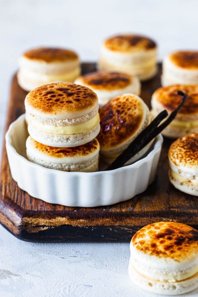Creme Brûlée Macarons inside of a ramekin, with the tops bruleed, with vanilla beans on the side.