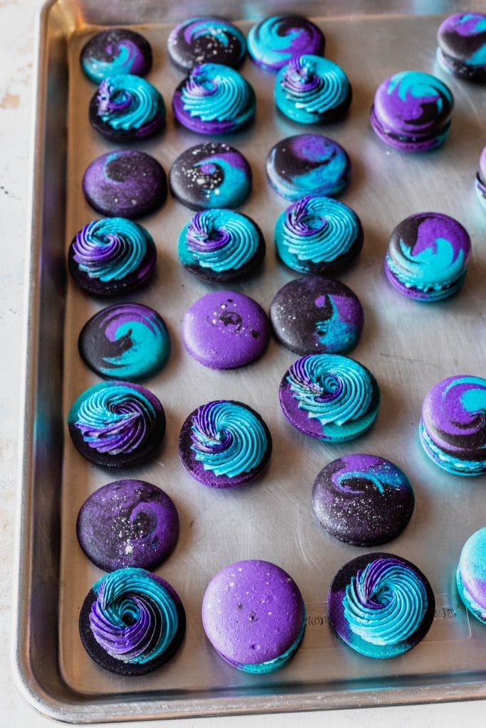 black macarons filled with a swirl frosting of black, blue and purple.