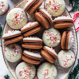 Peppermint Bark Macarons on a plate topped with white chocolate and crushed candy canes.