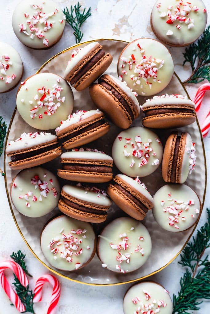 Peppermint Bark Macarons on a plate topped with white chocolate and crushed candy canes.