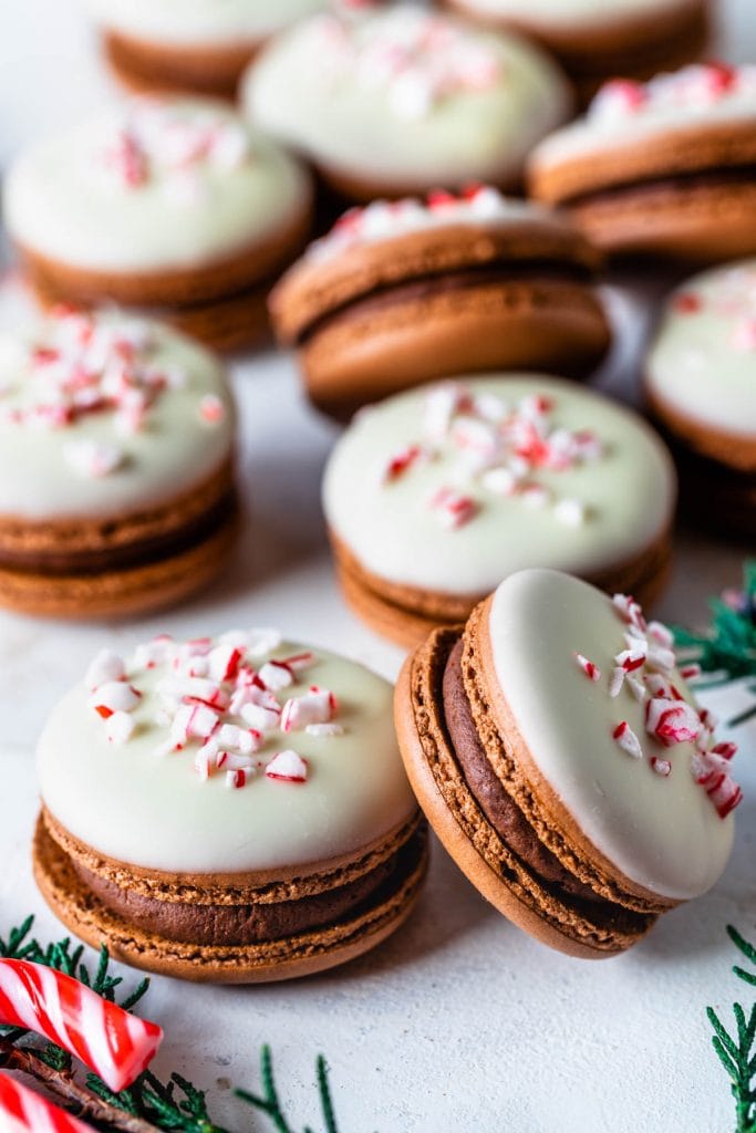 macarons filled with peppermint dark chocolate ganache and peppermint white chocolate ganache, topped with melted white chocolate and crushed candy canes, displayed on a plate.