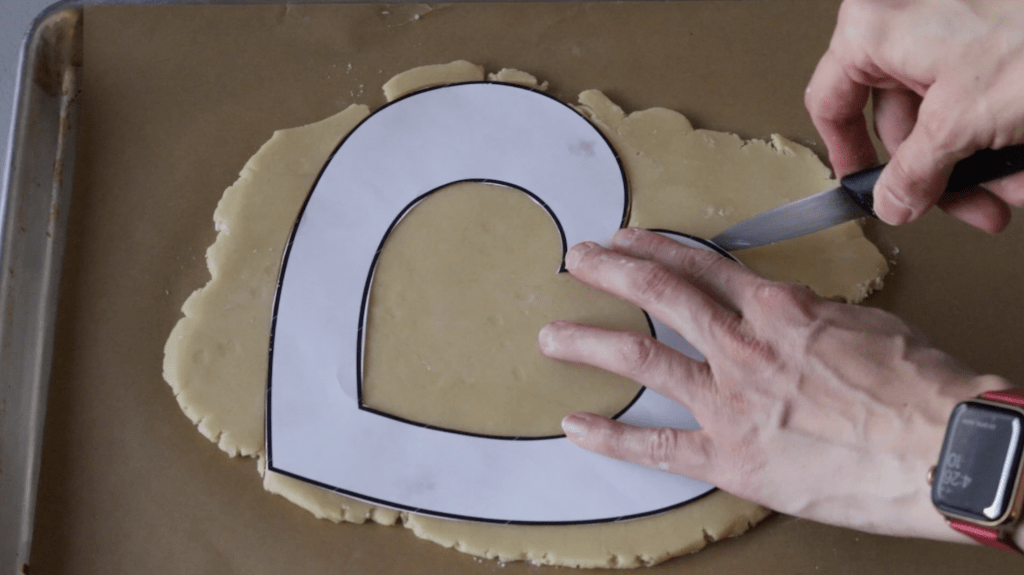 cutting out a heart shape out of cookie dough.