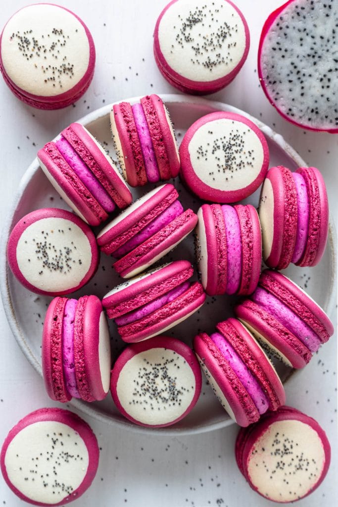 Pitaya macarons with a bicolor shell, pink and white, and with poppy seeds on top to resemble dragon fruit.