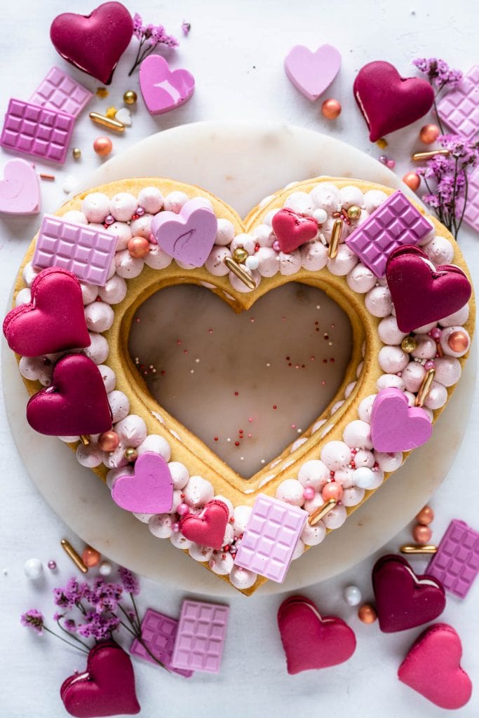 heart cookie cake topped with candy hearts, macarons, and sprinkles.