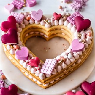 cookie cake shaped like a heart decorated with buttercream, macaron hearts, pink chocolate hearts.
