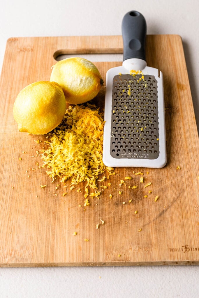 lemon zested on a cutting board next to a zester.