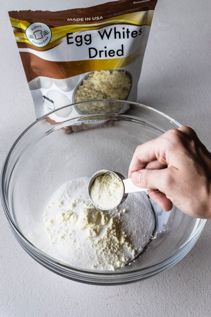 pouring egg white powder over granulated sugar in a bowl.
